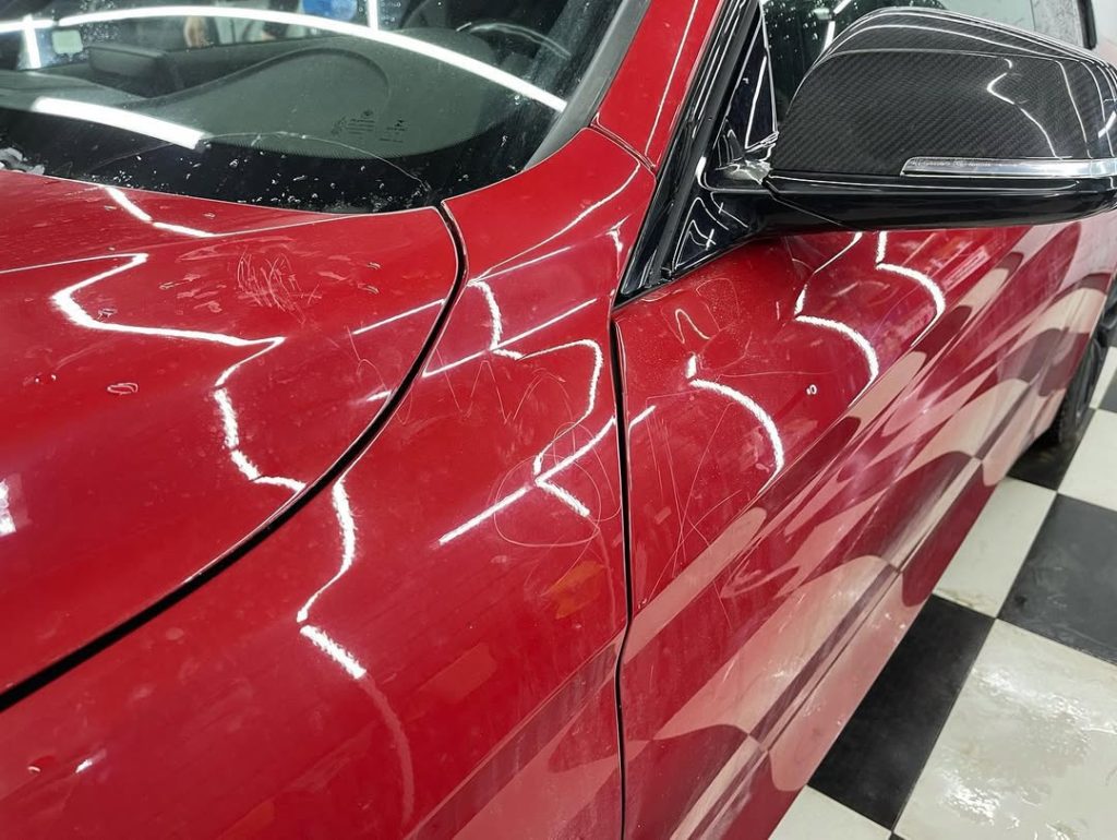 Close-up of a red car with scratches on the door panel, showing pre-detailing condition before professional scratch removal.