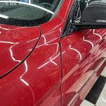 Close-up of a red car with scratches on the door panel, showing pre-detailing condition before professional scratch removal.