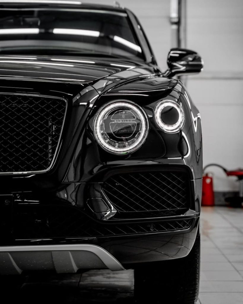Bentley front exterior detailed by AYB Detailing, showcasing polished headlight, grille, and glossy black paint with deep reflection and mirror-like finish.