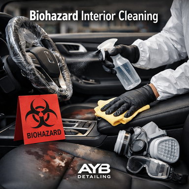 Person in protective gear cleaning a car interior with spray bottle and cloth, featuring biohazard sign and gas mask, detailed by AYB Detailing.