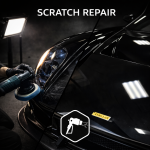 Mechanic polishing a scratched black car headlight with a buffer under bright light, showing professional scratch repair and detailing by AYB Detailing.