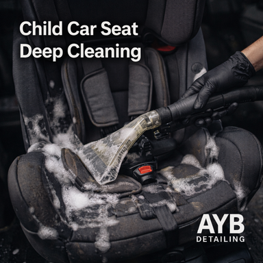 Gloved hand using a vacuum to deep clean a child car seat with soap suds, professionally detailed by AYB Detailing.