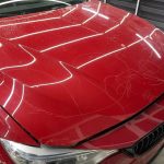 Close-up of a red BMW hood showing scratches before professional enhanced gloss finish and detailing by AYB Detailing.