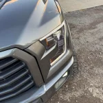 Close-up of a gray pickup truck front professionally detailed by AYB Detailing, highlighting a modern headlight design and chrome grille with a clean, reflective exterior finish under a clear sky.