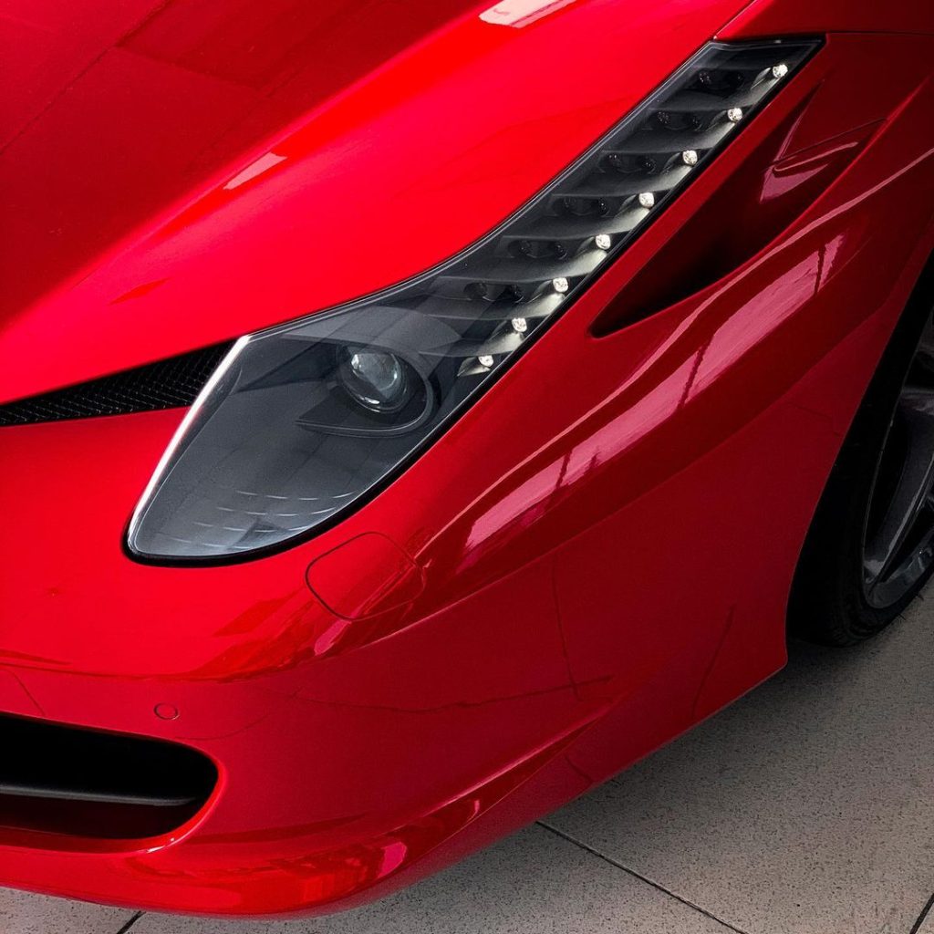 Close-up of a red Ferrari headlight and front fender after professional stainless steel polishing and detailing by AYB Detailing.